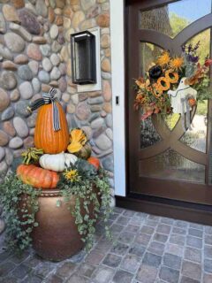 Colorful pumpkins and gourds tucked into a planter on a front porch