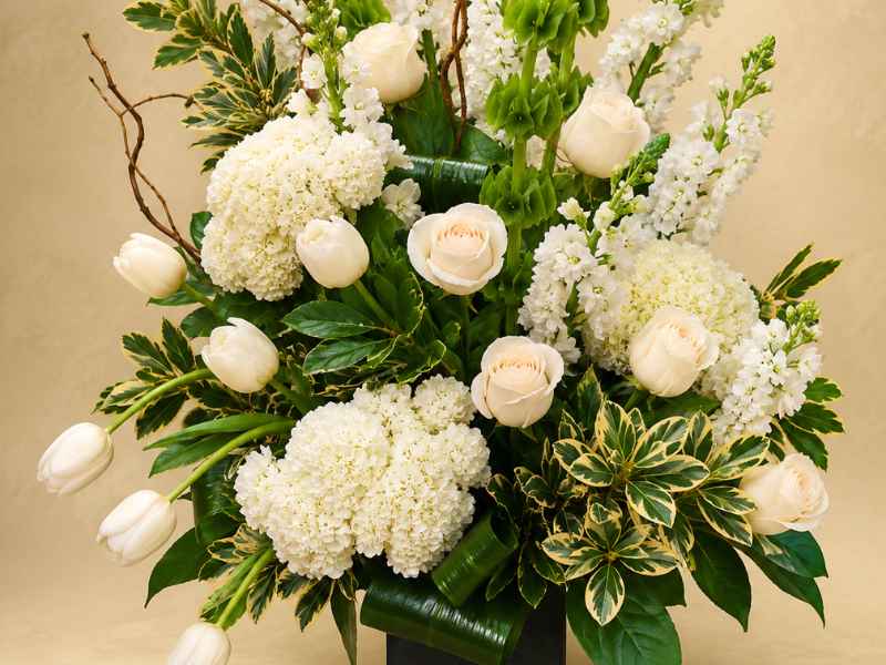 Funeral flowers with mixed white blooms and green leaves